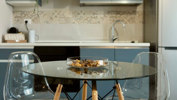 A modern kitchen with a glass dining table, two chairs, and a bowl of food on the table.