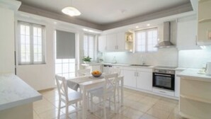 Una cocina moderna con muebles blancos, una mesa de comedor con sillas y un ventanal que proporciona luz natural.