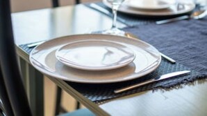 Una mesa de comedor dispuesta con platos, cubiertos y una copa.