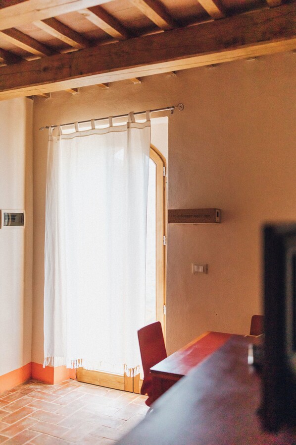 A room with a wooden ceiling, a white curtain, a wooden table, and red chairs. - Podere Biricocolo-Il Cortile- In the  countryside, 20 km from  Siena.  (Toscana)