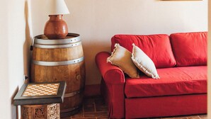 A cozy room with a red sofa, a wooden barrel, a small table with a chessboard, and a framed map on the wall. - Podere Biricocolo-Il Cortile- In the  countryside, 20 km from  Siena.  (Toscana)