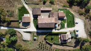 An aerial view of a residential area with multiple buildings, including a central house with a tiled roof, surrounded by smaller structures and a well-maintained lawn. - Podere Biricocolo-Il Cortile- In the  countryside, 20 km from  Siena.  (Toscana)