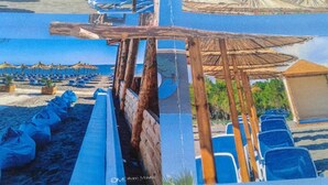 A beachside view with rows of blue chairs, wooden structures, and umbrellas. - Vila Elkom Apartment 9 (Ulcinj)