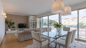 A modern living room with a sofa, a glass dining table, and a TV.