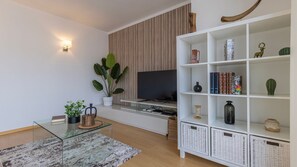 A modern living room with a flat-screen TV, a bookshelf, and a potted plant.