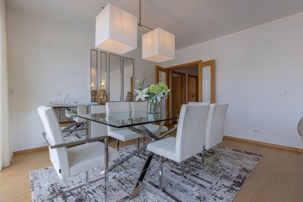 A modern dining area with a glass table, white chairs, and a central vase with flowers.