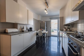 A modern kitchen with white cabinets, a granite countertop, a built-in oven, and a dining area with a table and chairs.