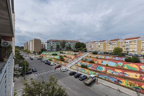 A street with colorful murals, parked cars, and residential buildings.