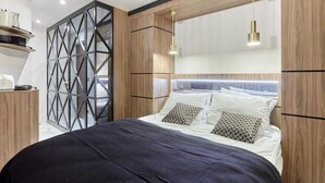 A modern bedroom with a geometric wall panel, a wooden headboard, and a bed with patterned pillows.