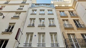 A multi-story building with a classical architectural style, featuring a central entrance with a triangular pediment, multiple windows with black railings, and a visible address number '8'.