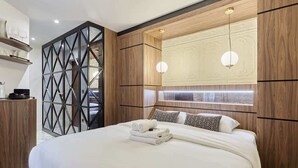 Ein modernes Hotelzimmer mit einem großen Bett, Holzvertäfelung, einem geometrischen Raumteiler und einer dekorativen Deckenleuchte.
