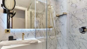 Une salle de bain moderne avec un lavabo en marbre, une douche à parois de verre et un robinet doré.