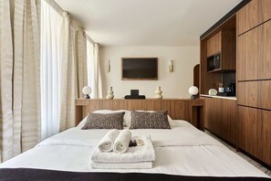 A hotel room with a large bed, wooden wardrobe, a flat-screen TV, and a small kitchen area. - Magnificent new studio Louvre - Palais Royal (Paris)