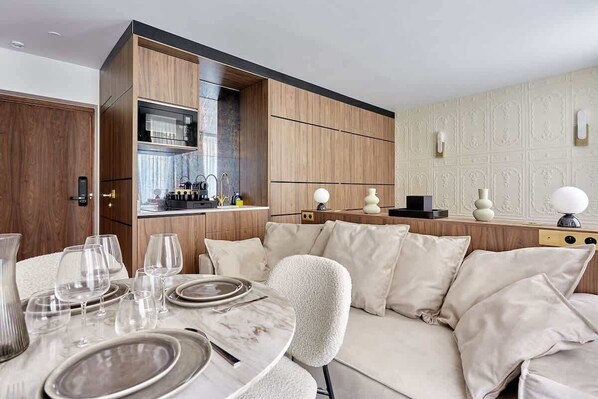 A modern kitchen with wooden cabinets, a built-in oven, and a dining area with a round table set for four. - Magnificent new studio Louvre - Palais Royal (Paris)