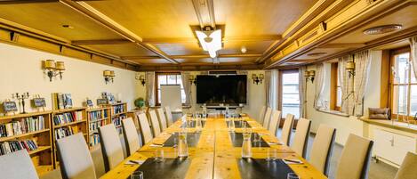 A conference room with a long table, chairs, bookshelves, and a television screen.