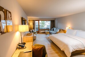 Ein Hotelzimmer mit einem großen Bett, einem Schreibtisch mit Lampe, einer Sitzecke und Blick ins Freie.
