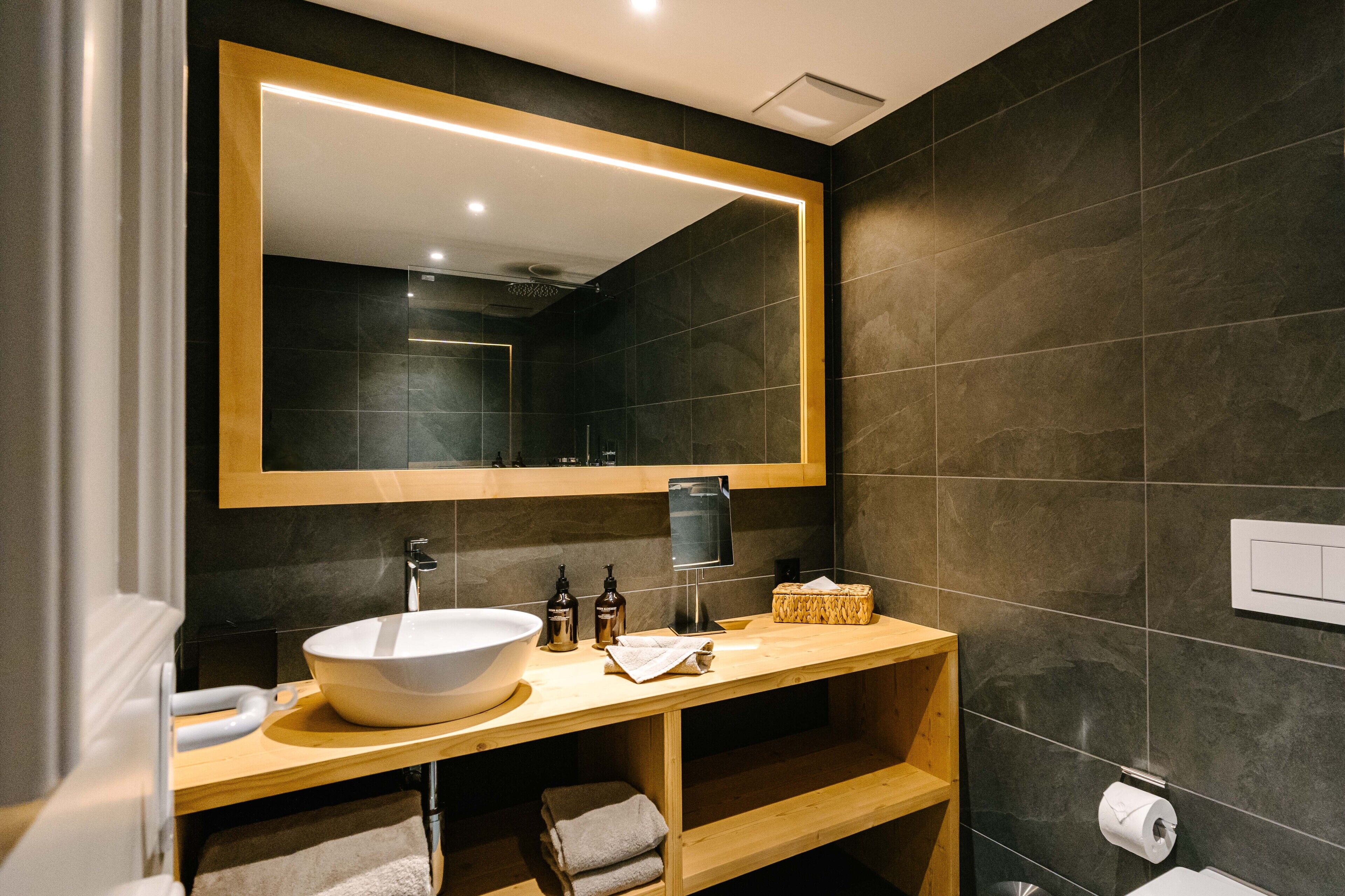 Un baño moderno con un espejo grande, un lavabo sobre encimera, estantes de madera y un perchero para toallas.