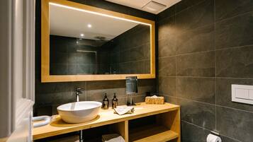 Un baño moderno con un espejo grande, un lavabo sobre encimera, estantes de madera y un perchero para toallas.