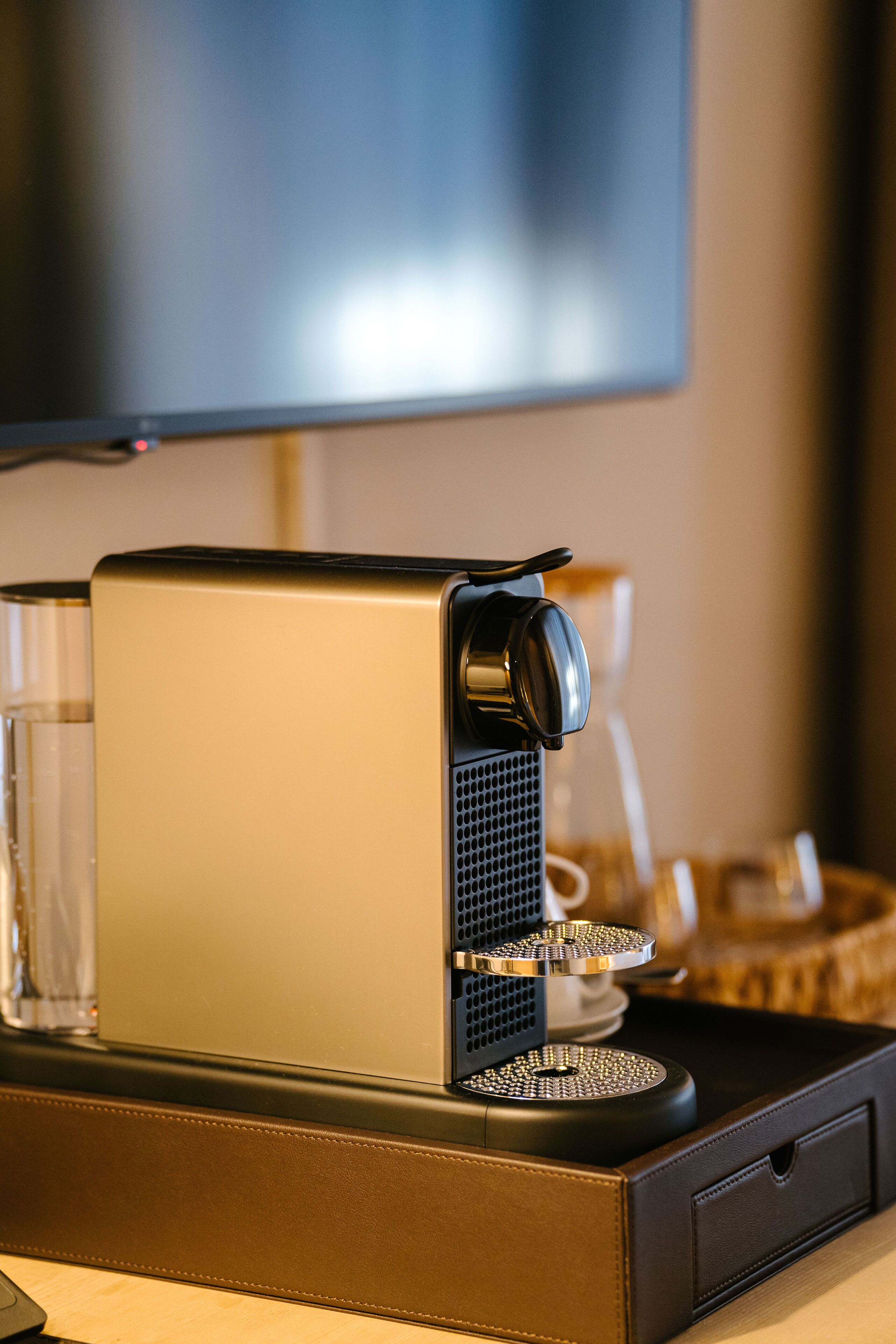 A coffee machine with a tray, glasses, and a basket on a table.