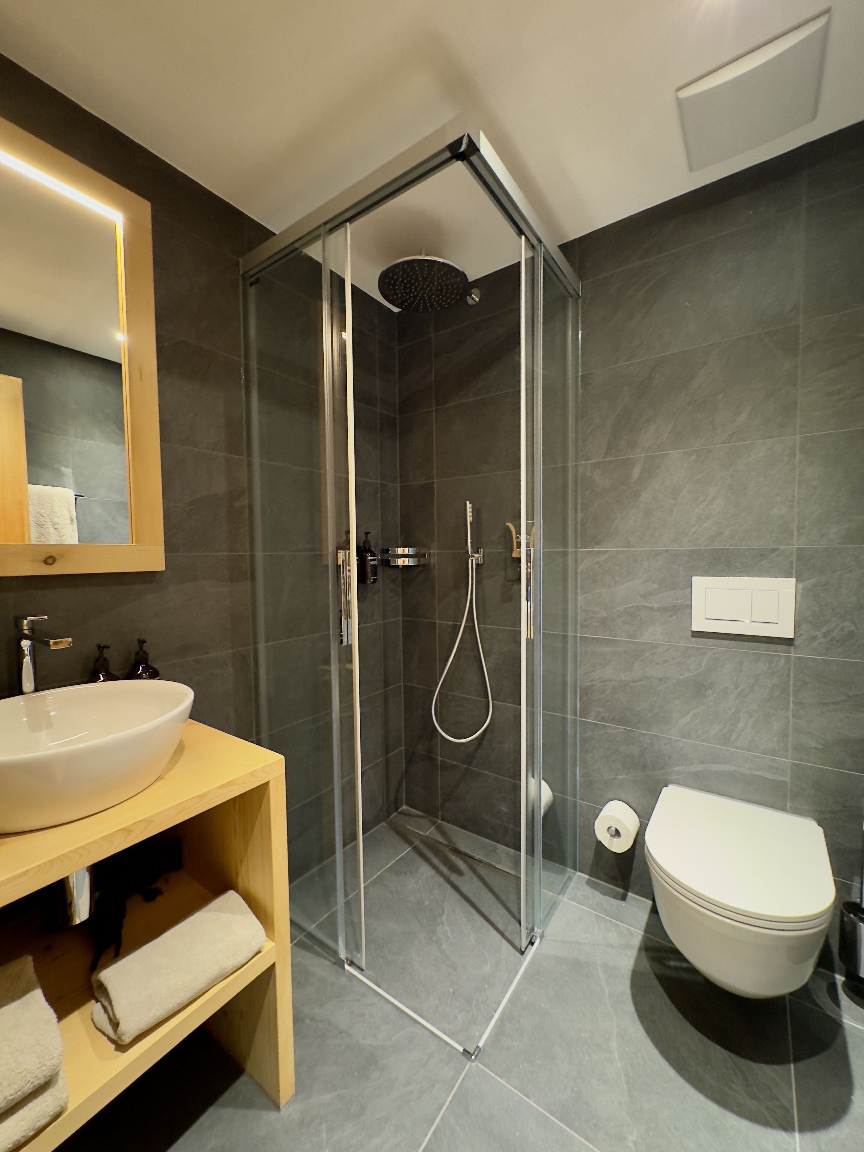 Un bagno moderno con doccia a vetro, mobile bagno in legno con lavandino e water.