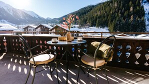 A balcony with two chairs and a table, overlooking a snowy mountain landscape. - Seven Alpina Boutique Hotel (Klosters-Serneus)