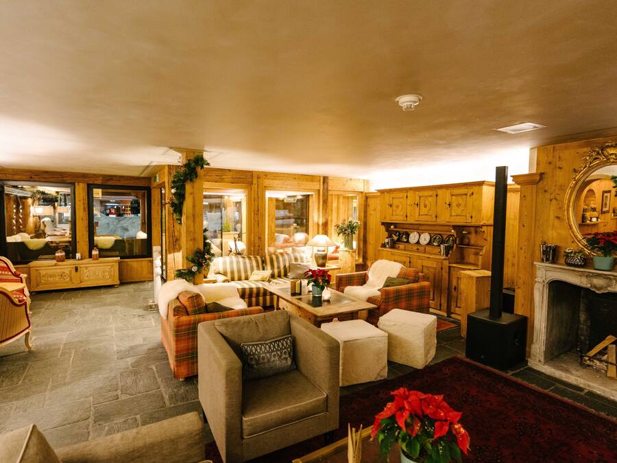 A cozy living room with wooden walls and a fireplace, furnished with sofas, armchairs, and a coffee table.