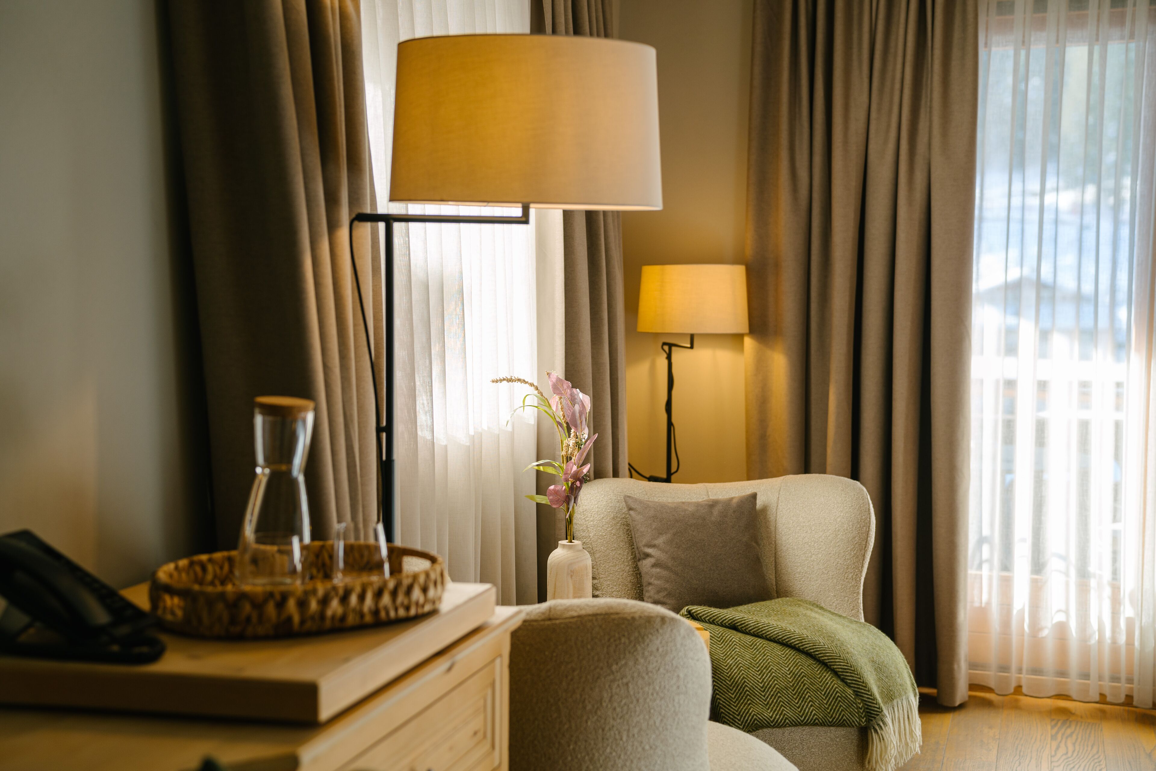 Habitación de hotel con sofá, lámpara, un jarrón con flores y teléfono sobre una mesita de madera.