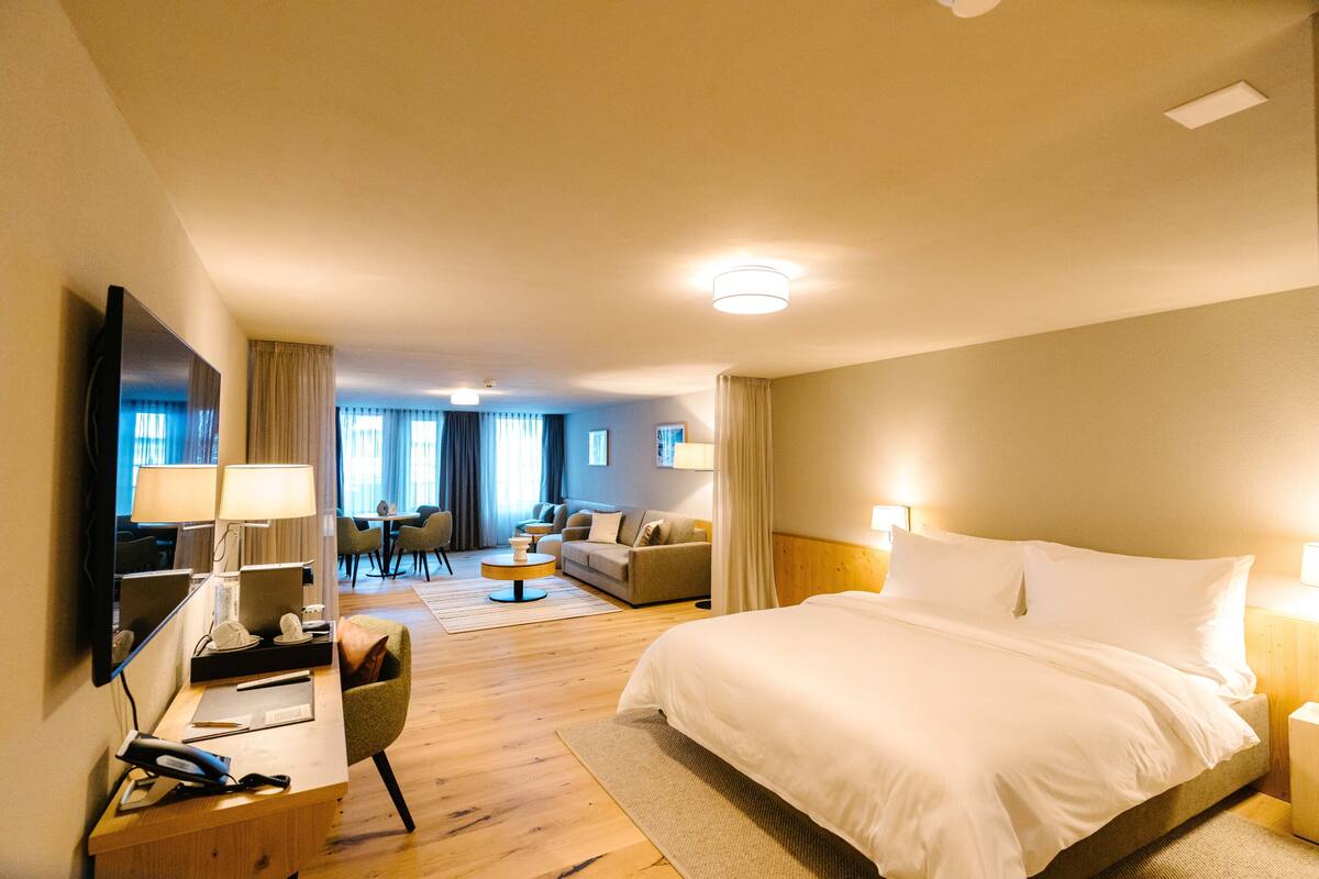 Habitación de hotel con una cama grande, un escritorio con teléfono y lámpara, una silla, un sofá y una televisión.