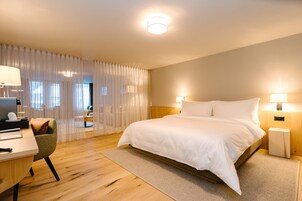 Una habitación de hotel moderna con una cama grande, un escritorio con una silla y vistas a la ciudad a través de cortinas traslúcidas.
