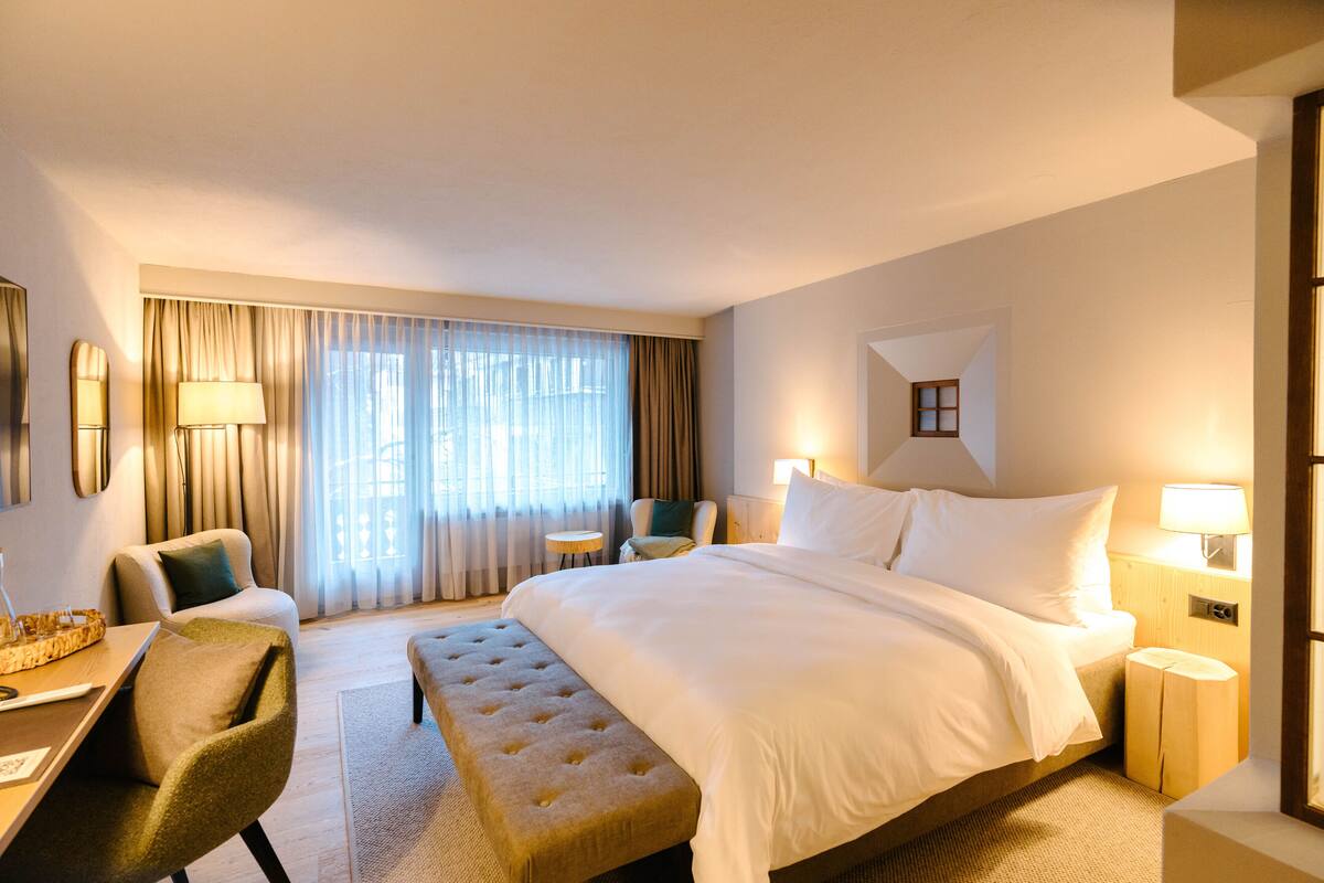 Habitación de hotel con una cama grande, un escritorio con silla, una mesita redonda y un banco.