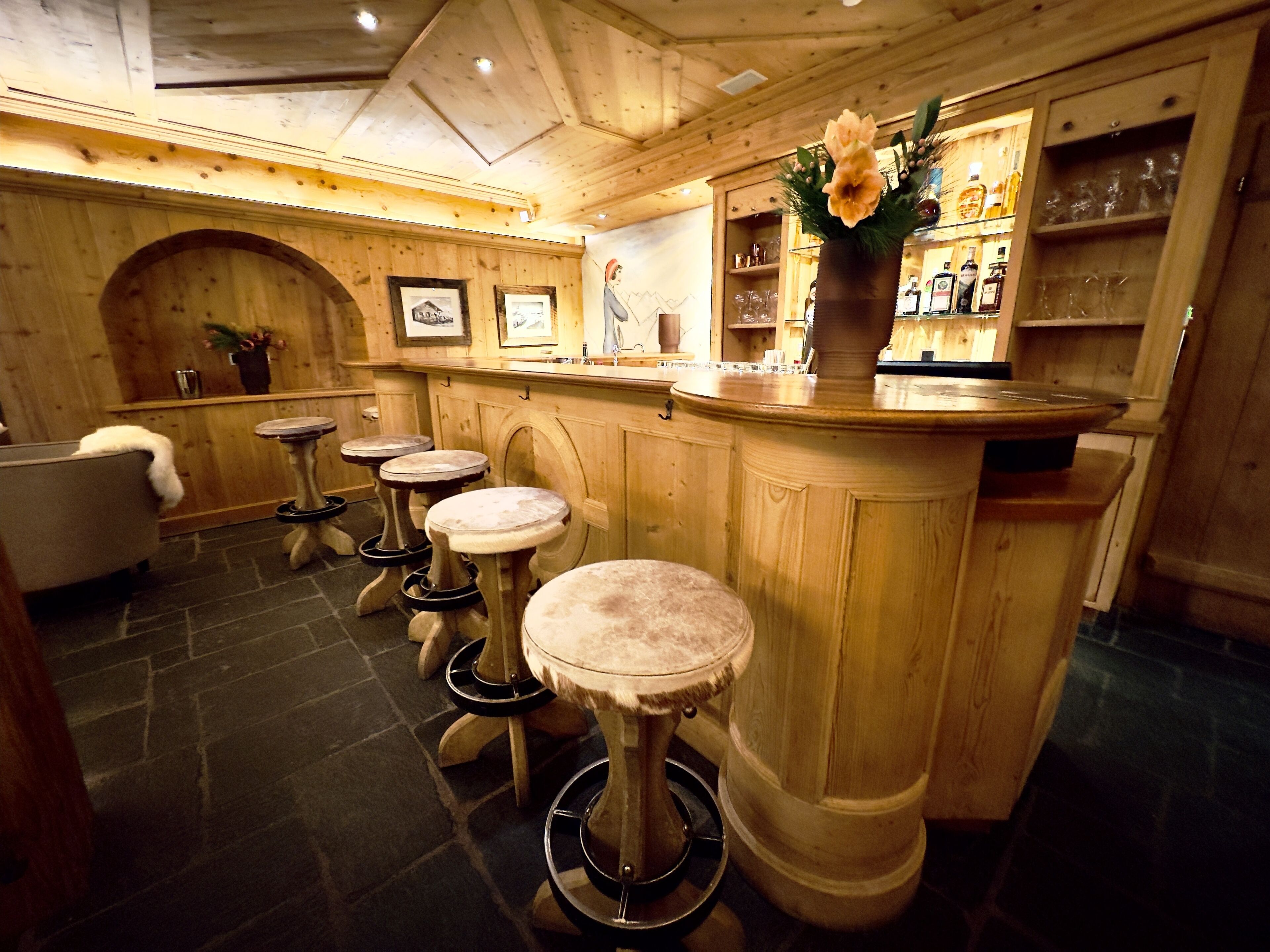 A bar area with wooden stools, a bar counter, and a flower vase.