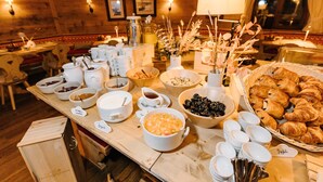 A buffet table with various food items and serving dishes, set in a room with wooden walls and a window. - Seven Alpina Boutique Hotel (Klosters-Serneus)