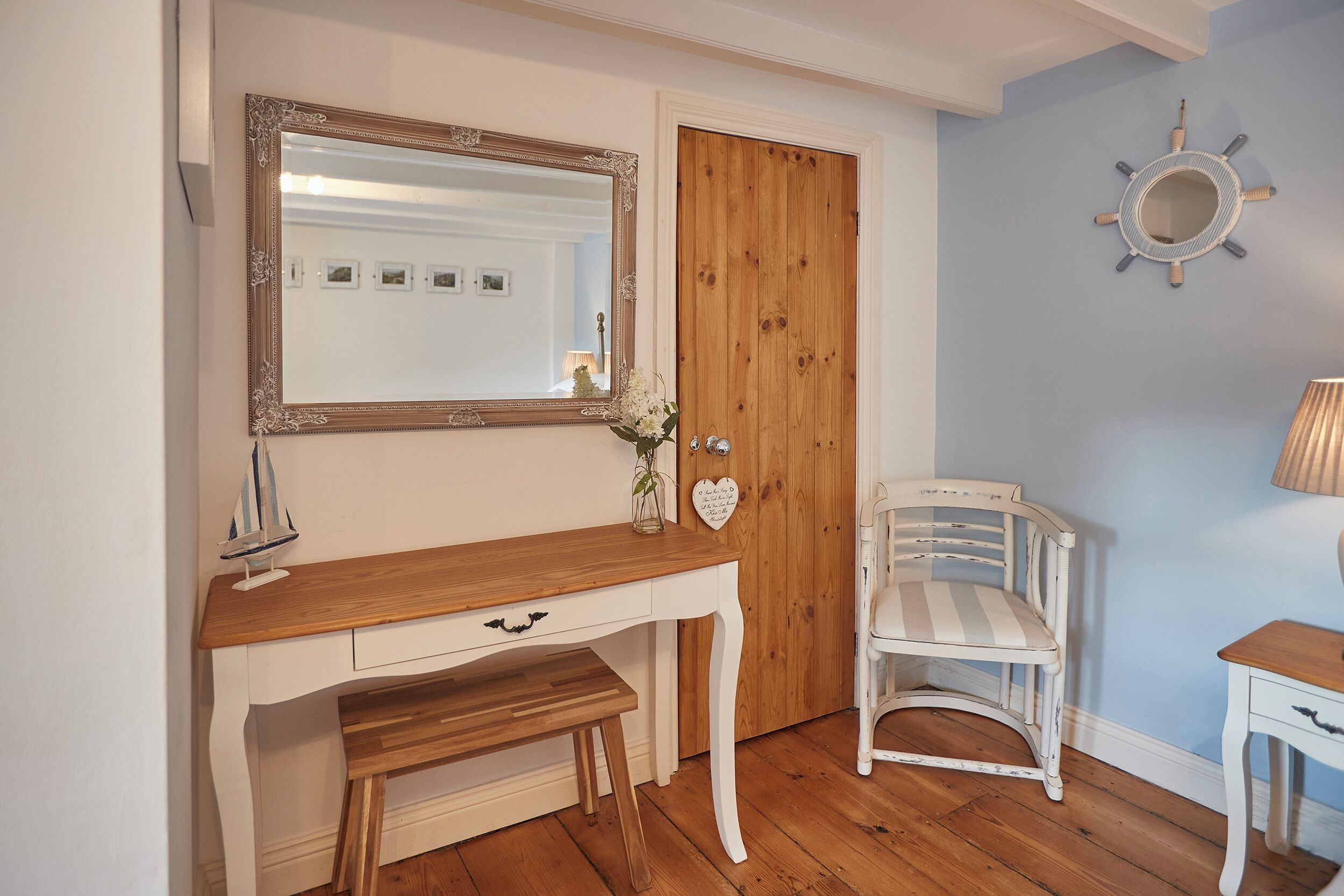 Ein Zimmer mit einem Holztisch, einem weißen Stuhl, einem Spiegel und einer Holztür.