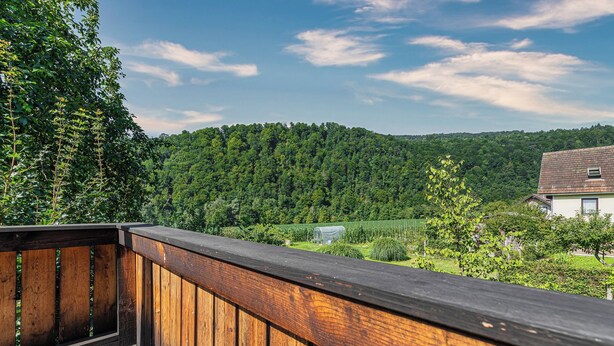 A wooden deck with a view of a green hillside and a house in the background.