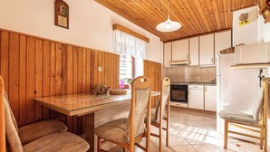 A wooden-paneled kitchen with a glass dining table, wooden chairs, and a hanging light fixture.