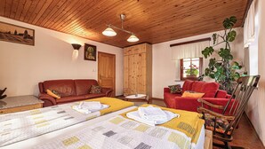 A cozy room with wooden ceiling, two beds with quilts, a red sofa, a wooden cabinet, and a large plant.