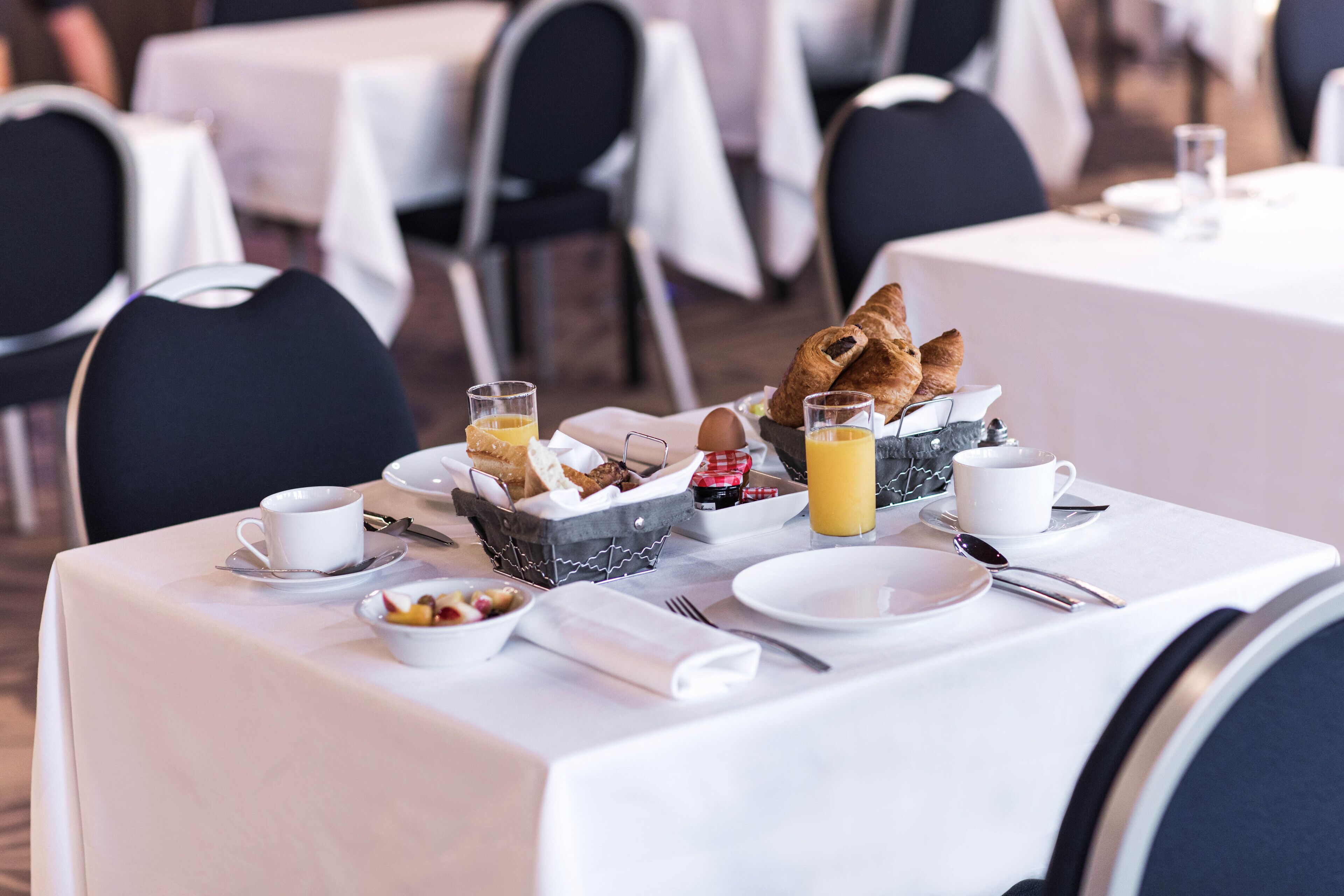 Un desayuno servido con una mesa para dos, incluyendo croissants, jugo de naranja y un bol de fruta.