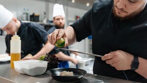 A chef preparing food in a modern kitchen with stainless steel surfaces and various cooking utensils.