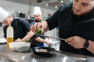 Un chef preparando comida en una cocina moderna con superficies de acero inoxidable y diversos utensilios de cocina.
