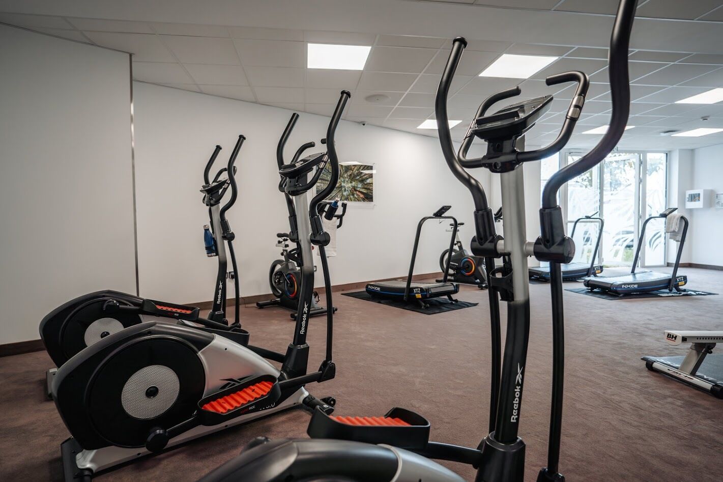 Une salle de sport équipée de divers appareils de cardio, notamment des tapis de course, un vélo elliptique et un vélo d’appartement.