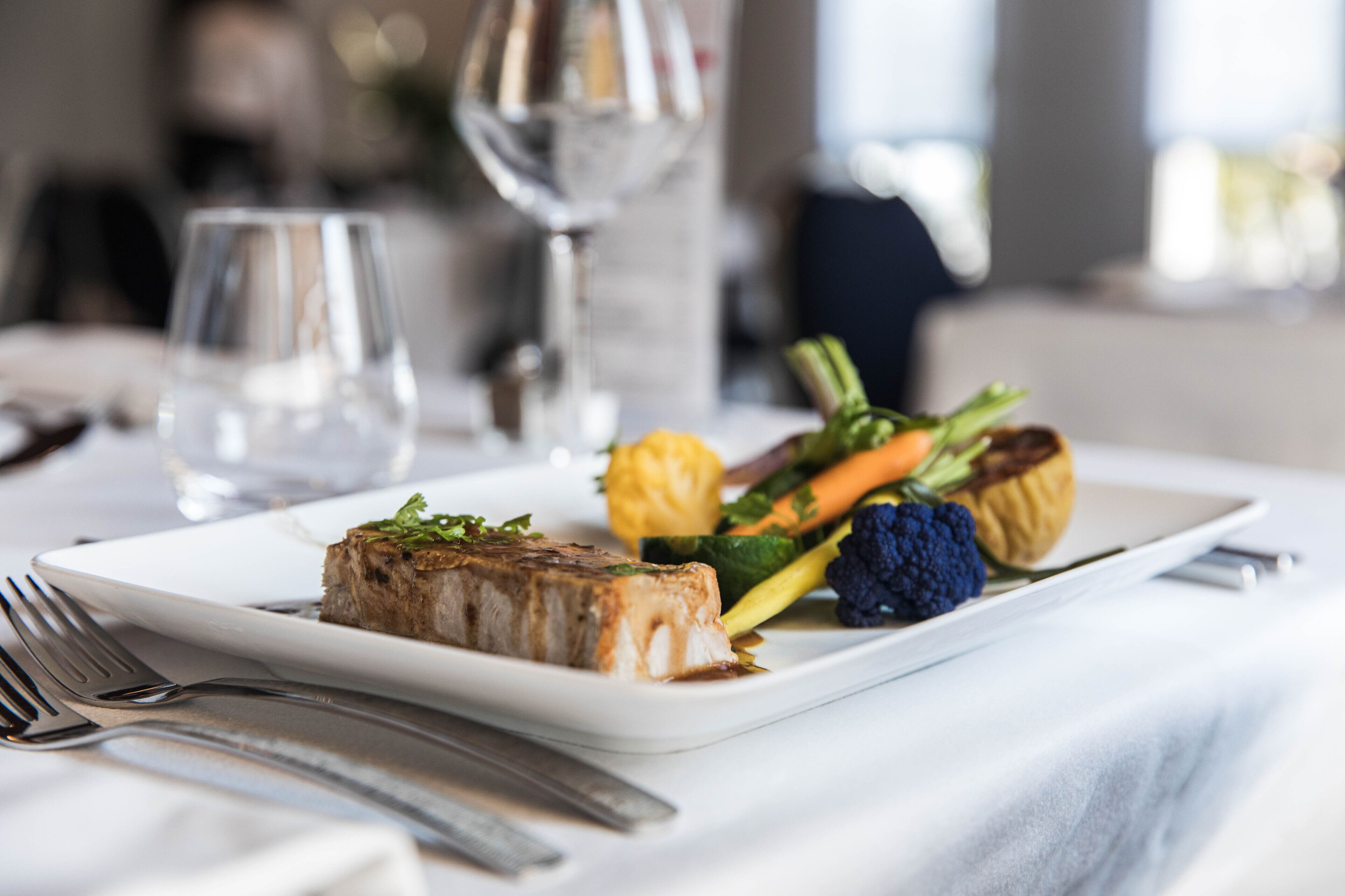 A plated meal with a piece of meat, vegetables, and a glass of water on a table.