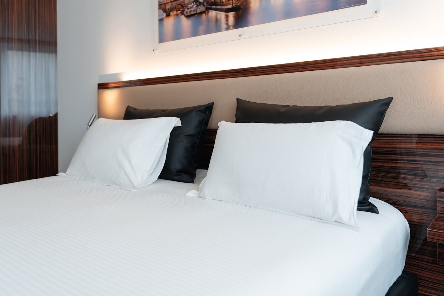 A hotel room with a large bed, two pillows, a headboard, and a framed picture on the wall.