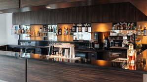 A modern bar area with a long counter, various bottles, and a coffee machine.