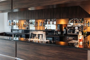 Un área de bar moderna con una barra larga, varias botellas y una máquina de café.