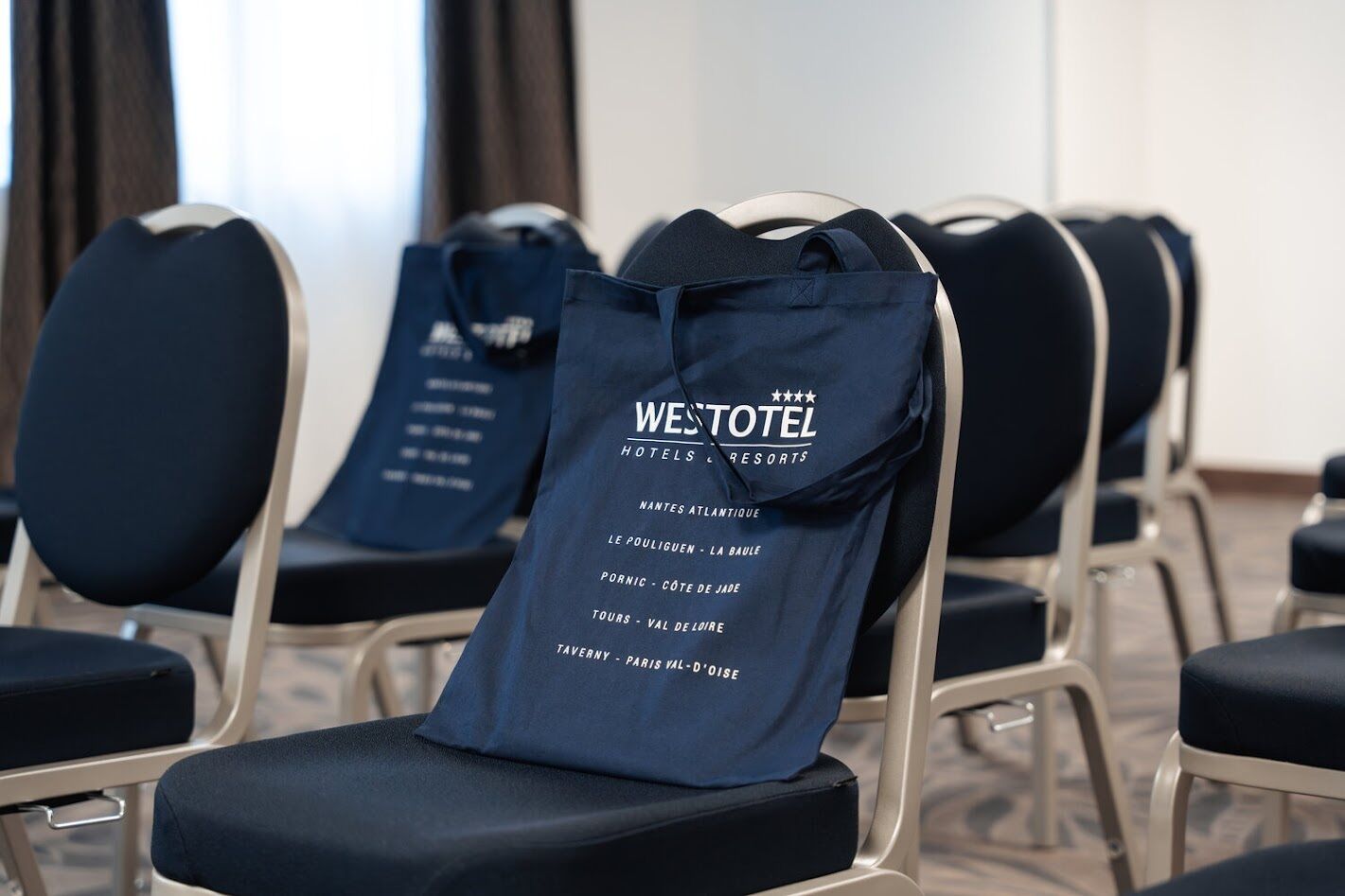 Rows of black chairs with a blue tote bag on one, listing WESTOTEL hotels and resorts.