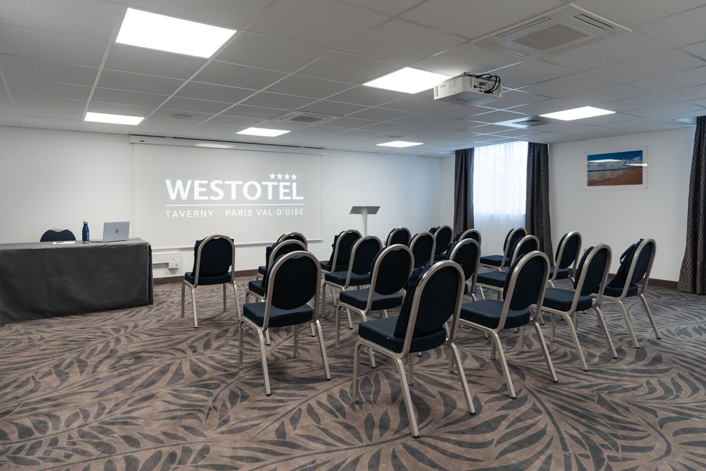 Uma sala de conferências com uma tela grande exibindo 'WESTOTEL TAVERNY - PARIS VAL-D'OISE' na frente.