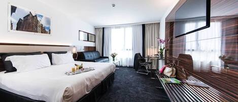 A hotel room with a bed, a desk, a chair, a sofa, and a TV.