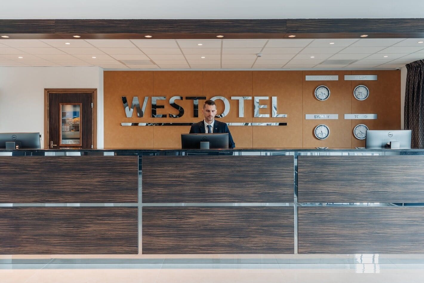 A reception desk at Westotel with a modern design, featuring a wooden panel backdrop and a digital display.