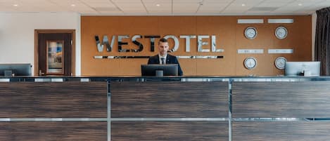 Un comptoir d’accueil au Westotel, doté d’un design moderne, avec un panneau mural en bois et un écran numérique.