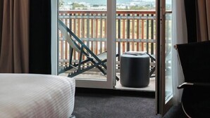 A hotel room with a bed, a chair, a small table, and a balcony with a view of the city.
